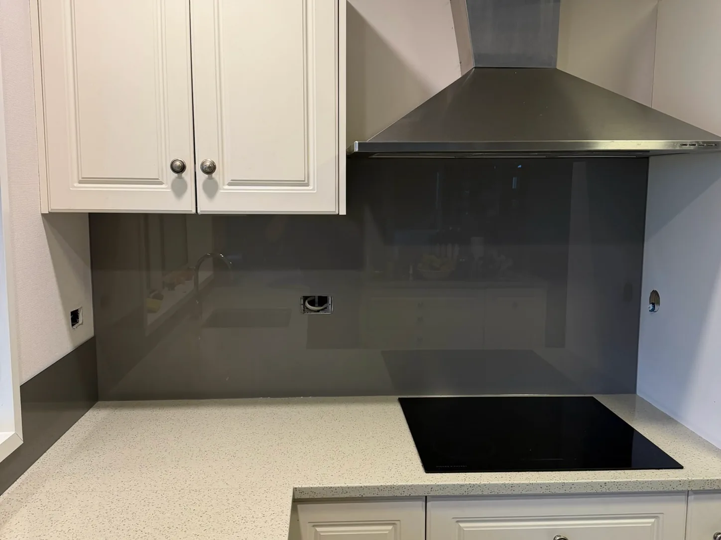 Dark grey glass splashback behind an induction cooktop and rangehood