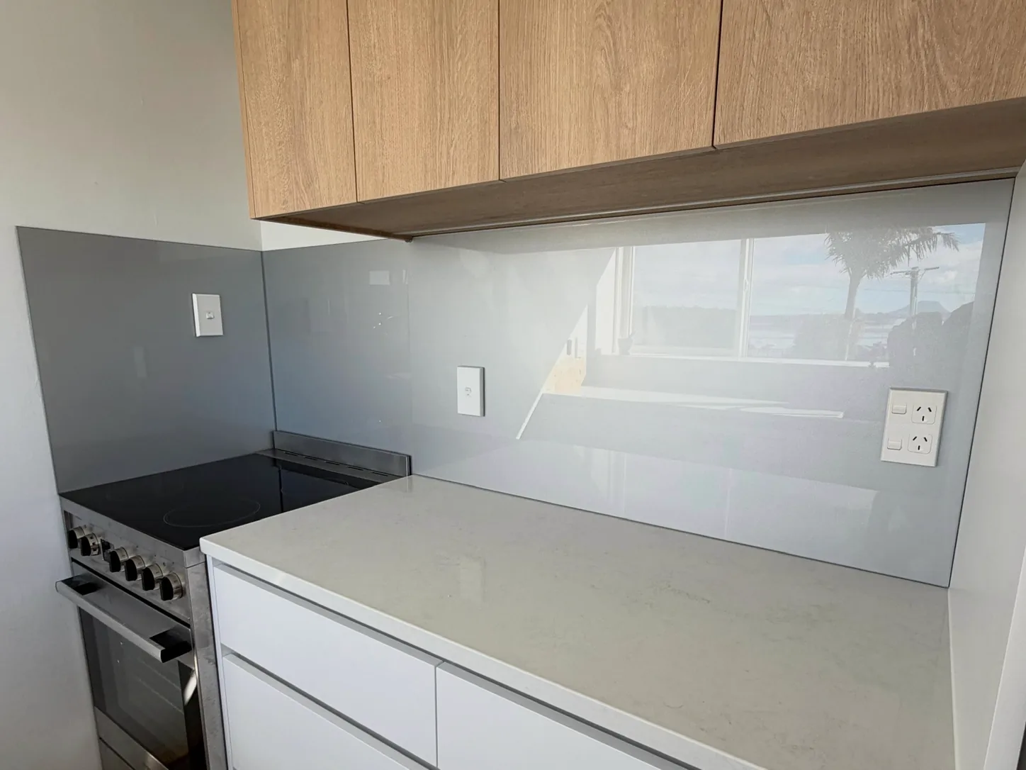 Pale grey glass splashback under timber cabinets beside a range